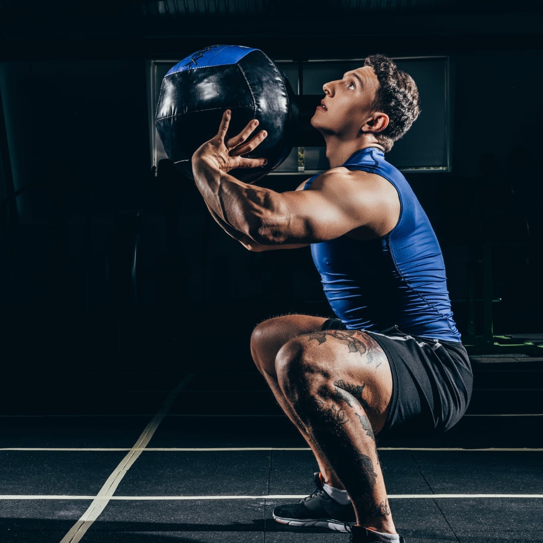 A man catching a medicine ball overhead as he rises out of a squat