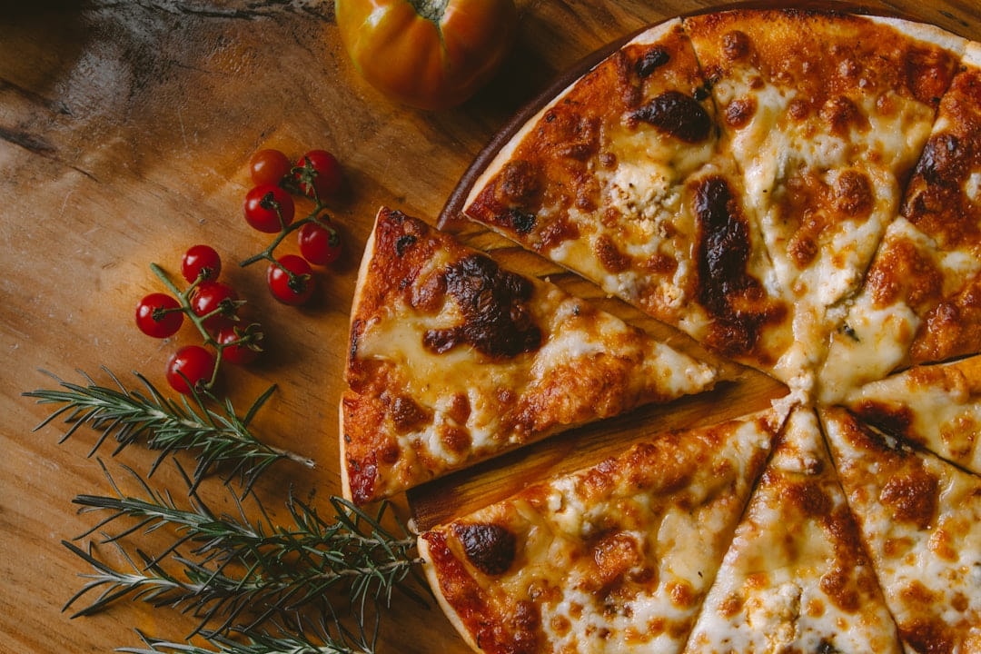 A sliced pizza on a wooden board with tomatoes and rosemary