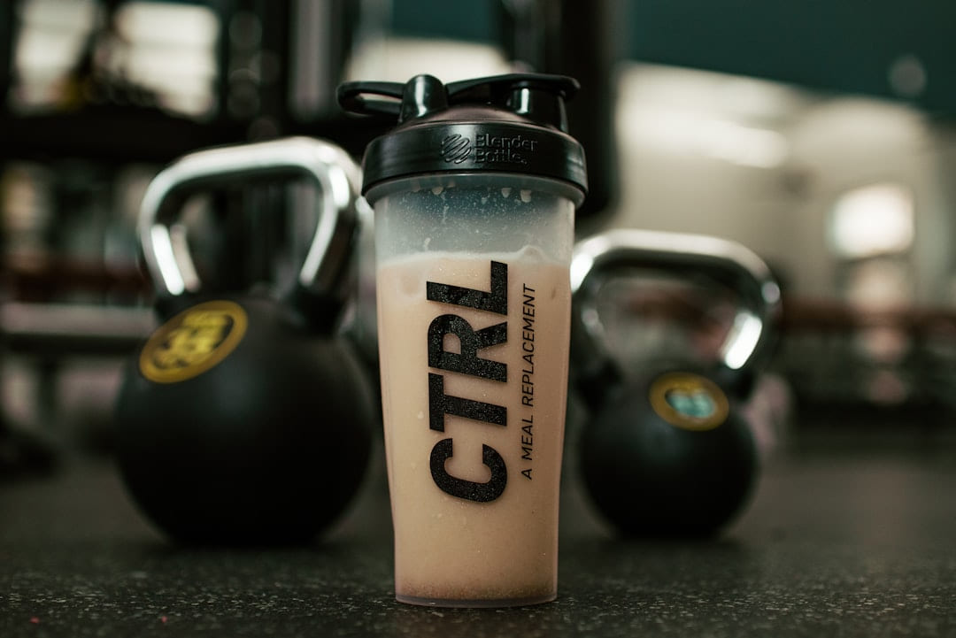 A shaker bottle of a meal replacement drink between kettlebells in a gym