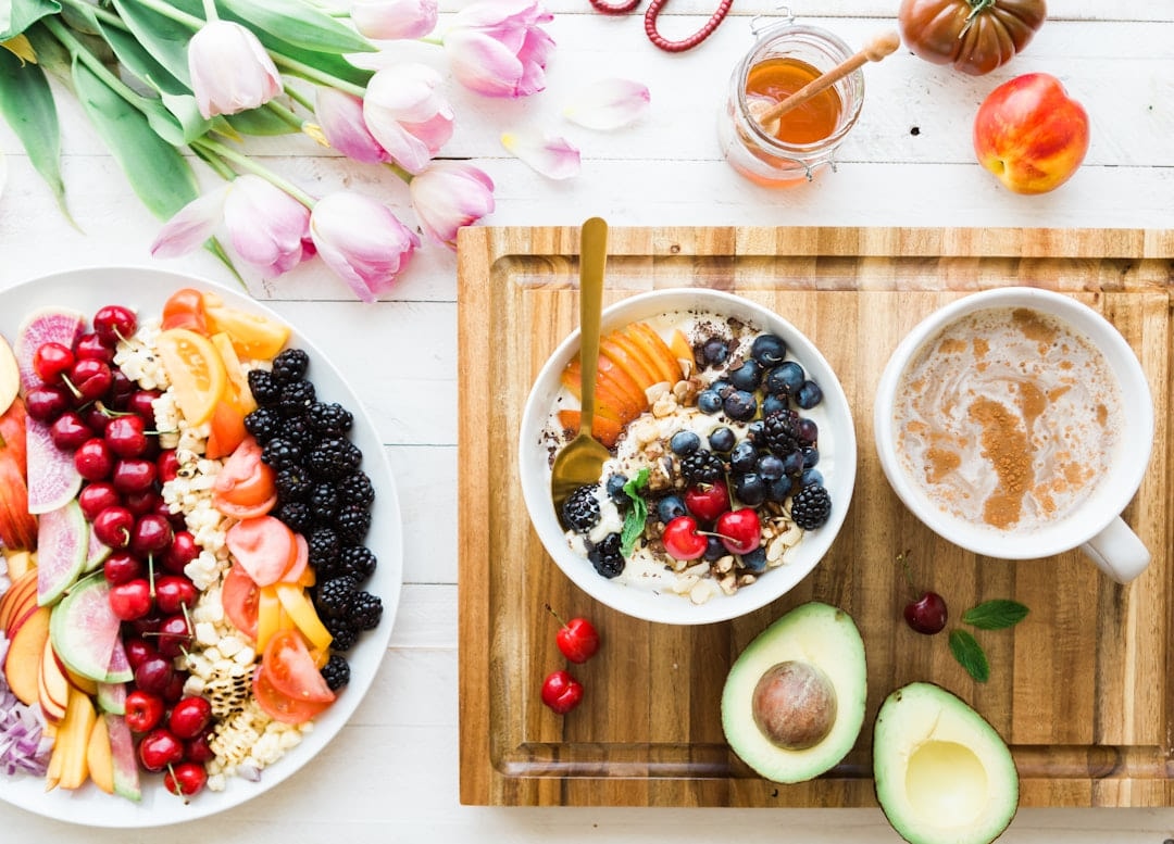 A breakfast spread of fruit, yoghurt bowls, avocado and coffee with tulips on the table