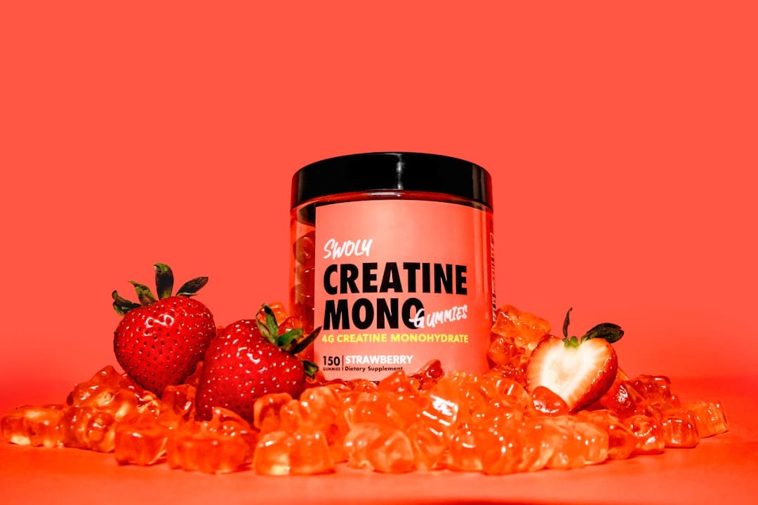 A tub of creatine monohydrate on a red background with strawberries