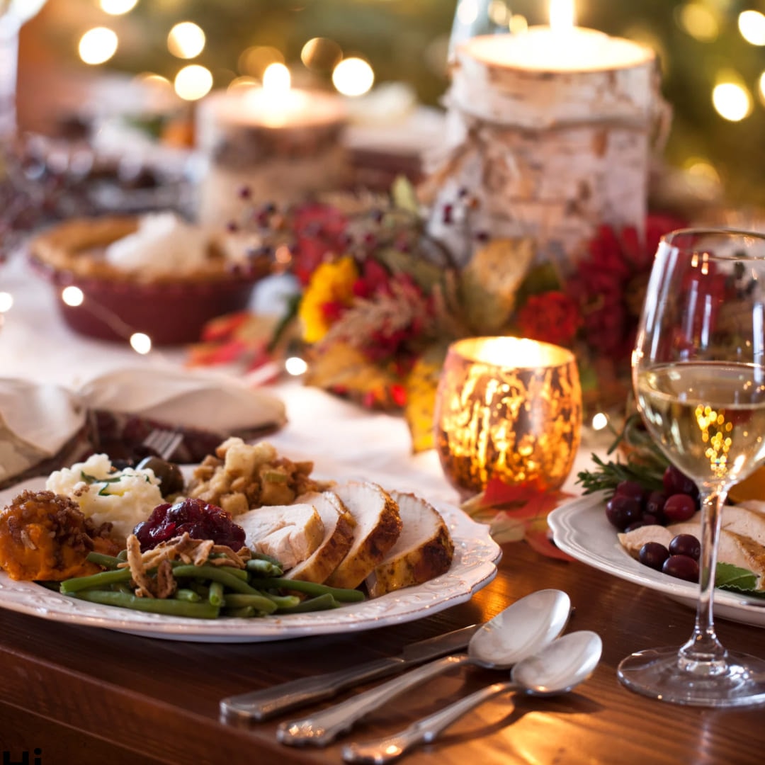 A festive dinner table laid with roast turkey, vegetables, candles and wine