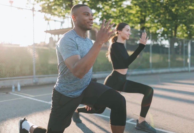 Two people training together outdoors, both mid-lunge